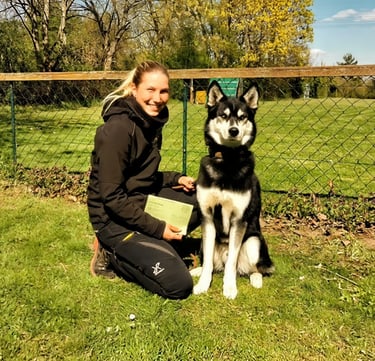 A smiling woman posing with her Alaskan Husky dog at an outdoor obedience training school.