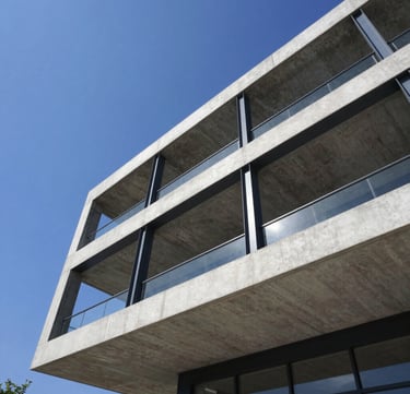 Low-angle portrait of a modern concrete and steel structure rising into a clear blue sky, clean geometric lines, bright daylight, high contrast