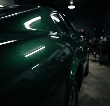 Macro detail of a flawless dark green metallic car paint finish reflecting dramatic workshop lighting, deep shadows, 50mm lens, rich metallic reflections.