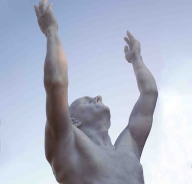 White marble statue of a man reaching his arms up toward a clear blue sky.