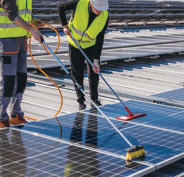 two men standing on a roof using mops to clean solar panels