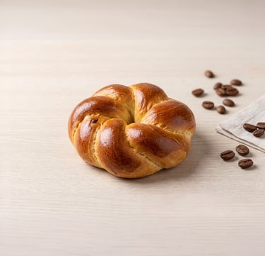 Golden brown braided brioche bun on a wooden surface with scattered roasted coffee beans.