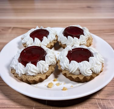 Cuatro mini tartas de frutas con centros de gelatina roja y glaseado de crema batida en un plato bla