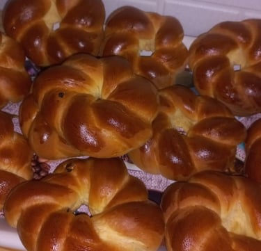 A batch of golden brown freshly baked braided brioche rolls on a cooling rack.