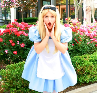 Surprised performer in an Alice in Wonderland blue dress costume posing by pink roses.