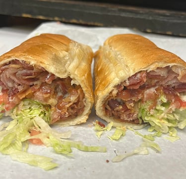 Hot toasted sub sandwich with crispy bacon, shredded lettuce, and tomatoes on white paper.