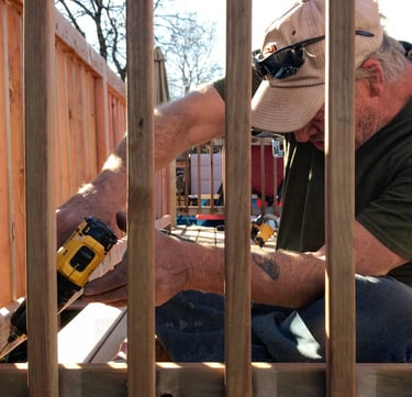 Brewer Construction carpenter installing new deck balusters on an Evergreen property with a power drill.
