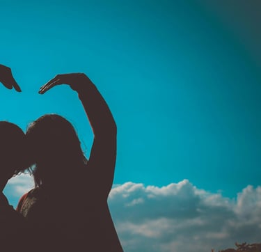 deux silhouettes regardant l'horizon bleu et formant un coeur avec leurs bras