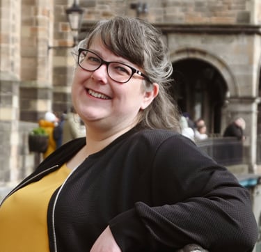 Laura is leaning against a railing and smiling at the camera