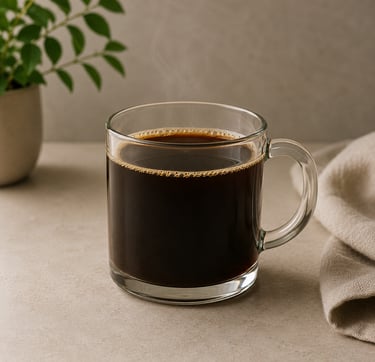 Steaming hot black coffee in a clear glass mug on a stone countertop with a green plant.