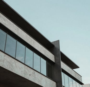 A minimalist architectural detail of a contemporary building in a Brazilian urban center. The composition focuses on clean lines and sharp angles of dark grey steel and light grey concrete. A soft baby blue sky is reflected in the polished glass surfaces, creating a serene and innovative atmosphere.