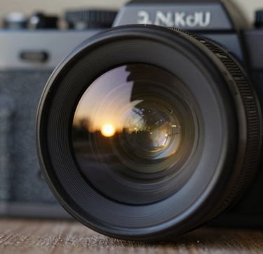 A close-up, artistic shot of a vintage camera lens reflecting a sunset scene. The glass of the lens catches glints of #C4B29A and #F5F0E1, while the body of the camera is a deep #262626. The focus is sharp on the reflections, capturing the 'moment' within the gear itself. The style is premium, sophisticated, and rich with texture.