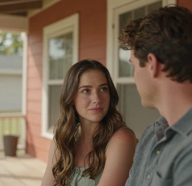 A close-up, candid photograph of an authentic couple sharing a quiet, sun-drenched moment on a wooden porch of a North American / US home. The composition is intimate and cinematic, featuring warm terracotta accents in the background. The lighting is soft and natural, highlighting genuine emotion and connection.