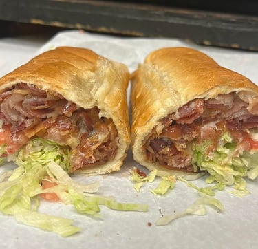 Hot toasted sub sandwich with crispy bacon, shredded lettuce, and tomatoes on white paper.