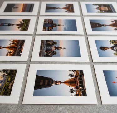 An editorial close-up photograph of high-end photography prints laid out on a soft gray stone surface. The composition is strictly grid-based and highly organized. Soft, natural daylight illuminates the textures of the archival paper. Global / Contemporary Art setting. The mood is professional and curated, using a palette of off-white and muted tones.