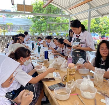 a large group of students sitting at a table making pottery