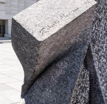 Granite stone sculpture with the signature of artist Roberto Manzano carved into the surface.