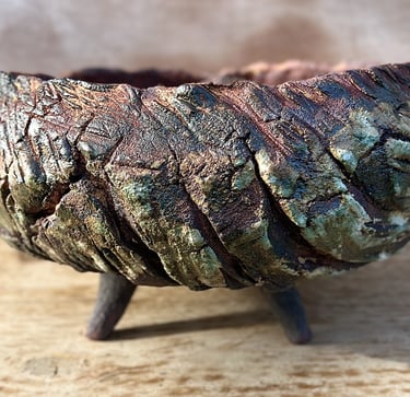 A large ceramic plant pot with 4 conic legs glazed in green and brown with wooden like texture