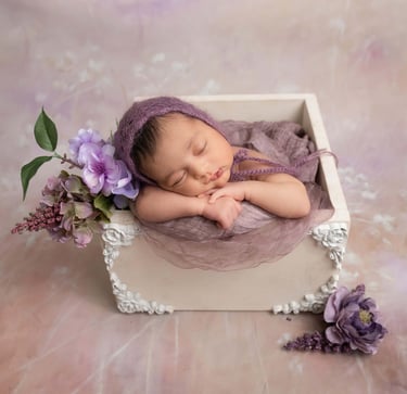 a newborn girl sleeping in a box with purple flowers