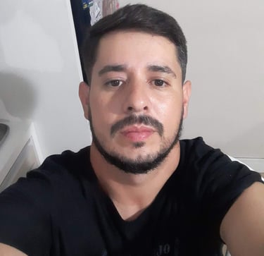 A high-angle selfie of a young man with a dark beard and mustache wearing a black t-shirt.
