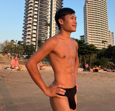 Man standing confidently on Pattaya Beach at sunset, with tall modern buildings and palm trees in the background.