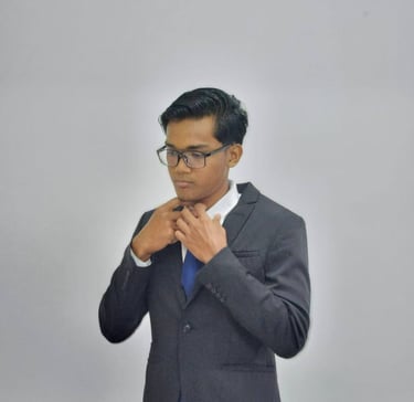 Professional young man in a charcoal suit and blue tie adjusting his collar against a gray background.