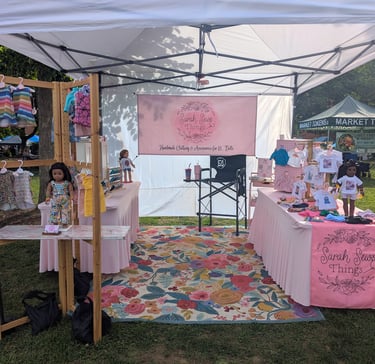 Image shows a market booth with doll clothes for sale