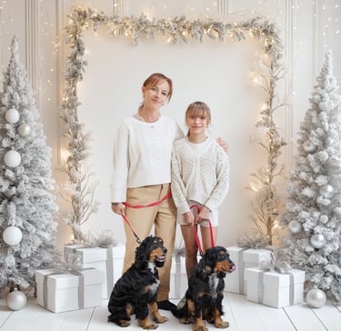 Mother and daughter posing with two spaniel dogs in a white winter holiday studio setting with lights.