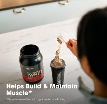 Person pouring a scoop of Gold Standard Whey protein powder into a shaker bottle to build muscle.