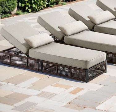 Wicker outdoor lounge chairs with beige cushions on a stone patio poolside.