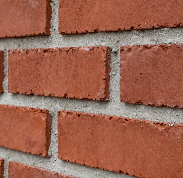 A sharp, close-up photograph of premium masonry work. Deep brick red bricks are laid with meticulous precision, separated by clean, even lines of soft light grey mortar. The lighting is direct and clear, emphasizing the robustness and texture of the craftsmanship.