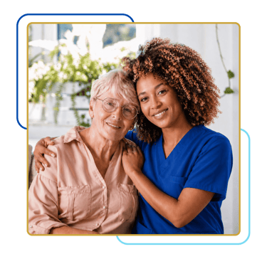 Smiling caregiver in blue scrubs embracing a senior woman, showing compassionate support in a bright home setting