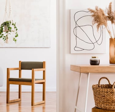 Doorkijkje in kamer met vierkante houten stoel in het midden, een sterachtige plant linksvoor.