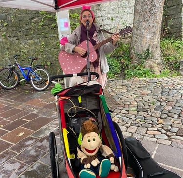 Sängerin Betti mit rosa Gitarre und Kinderwagen in der Tiengener Altstadt. Handpuppe sitzt im Wagen.