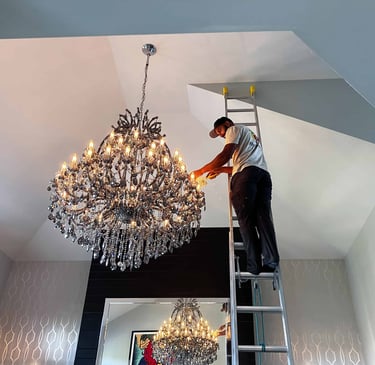Mop Monkey technician dusting crystal chandelier from ladder in Calgary