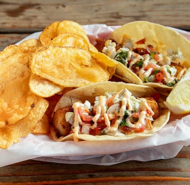 Fish tacos with cabbage, tomatoes, and sauce served with potato chips and a lemon wedge from Captain’s Galley