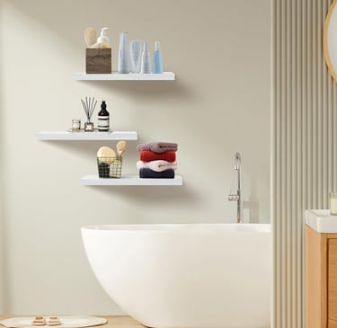 White floating wall shelves in a bathroom above a bathtub holding towels and toiletries.