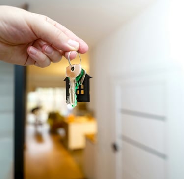 Una mano che impugna le chiavi di casa con un portachiavi in un moderno e luminoso salotto.