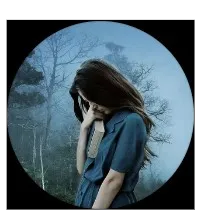 Mid shot of a young woman with long dark hair looking down and holding a book - image is framed by a black vignette