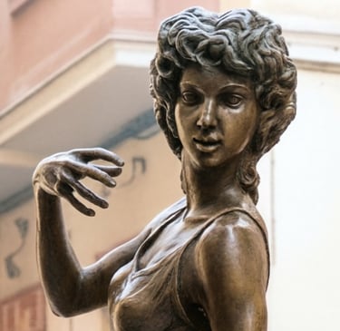 Bronze statue of a female dancer with curly hair and hand raised in a graceful pose.