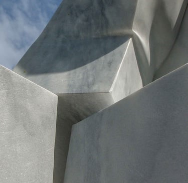 Abstract white marble sculpture with geometric stone shapes and sharp shadows against a blue sky.