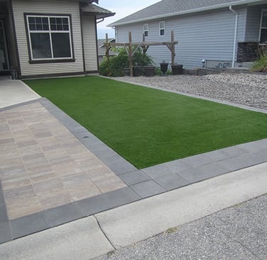 a front yard patio with a paver walkway and synthetic grass