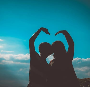 deux silhouettes regardant l'horizon bleu et formant un coeur avec leurs bras