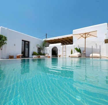 Luxury villa swimming pool with white architecture, turquoise water, and loungers under a blue sky.