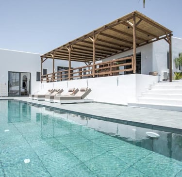 Luxury white villa with a private infinity pool, sun loungers, and a wooden pergola terrace.