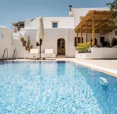 Luxury Greek villa with a sparkling blue infinity pool and sun loungers under a white Cycladic house.