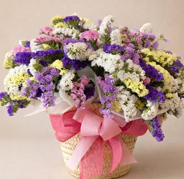 A colorful bouquet of purple, pink, and white dried statice flowers in a woven basket with a pink ribbon.
