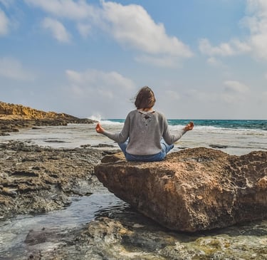 A woman meditating on a rock in front of the sea. 