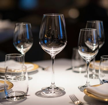Elegant table setting in a high-end restaurant featuring premium glassware and minimal golden accents, dramatic side-lighting, 35mm