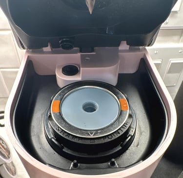 Inside view of a pink Keurig coffee maker pod holder with sharp needle and filter assembly.